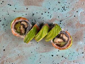 Caterpillar z węgorzem w środku, łososiem i avocado na zewnątrz, polane słodkim sosem, posypane sezamem